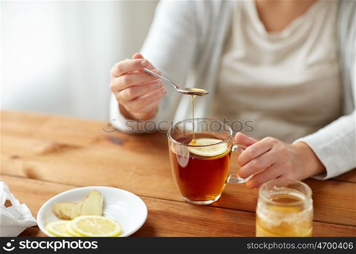 health, traditional medicine and ethnoscience concept - close up of ill woman drinking tea with lemon, honey and ginger at wooden table