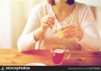 health, traditional medicine and ethnoscience concept - close up of ill woman drinking tea with lemon and honey at wooden table. close up of ill woman drinking tea with honey