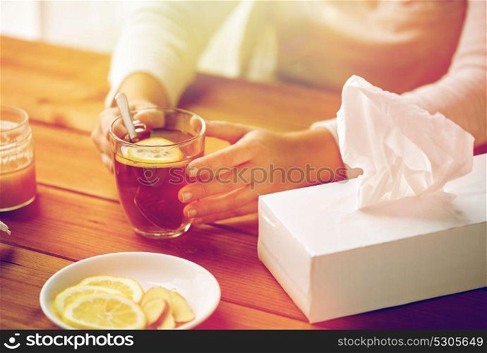 health, traditional medicine and ethnoscience concept - close up of ill woman drinking tea with lemon, honey and ginger at wooden table. close up of ill woman drinking tea with lemon