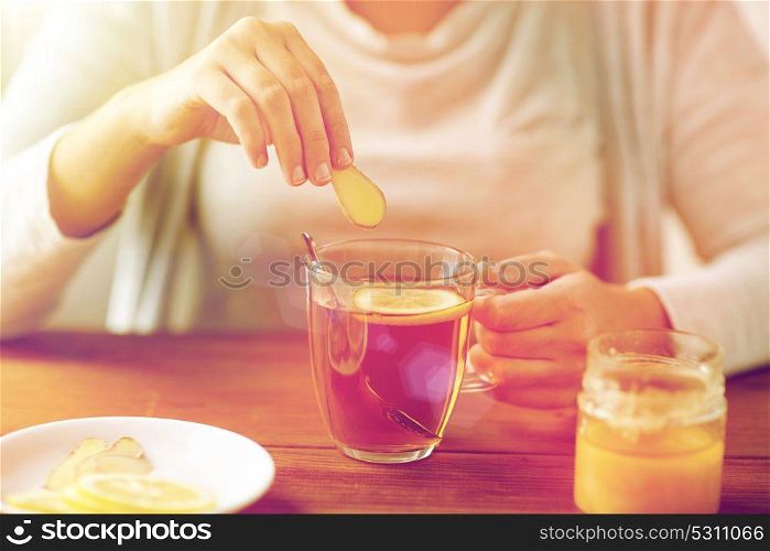 health, traditional medicine and ethnoscience concept - close up of ill woman drinking tea with lemon, honey and ginger at wooden table. close up of ill woman drinking tea with ginger