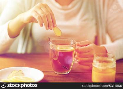 health, traditional medicine and ethnoscience concept - close up of ill woman drinking tea with lemon, honey and ginger at wooden table. close up of ill woman drinking tea with ginger