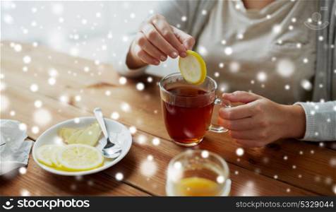 health, traditional medicine and ethnoscience concept - close up of ill woman adding lemon to tea cup over snow. close up of ill woman adding lemon to tea cup