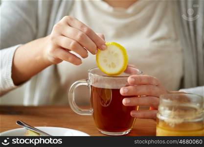 health, traditional medicine and ethnoscience concept - close up of woman adding lemon to tea cup with honey
