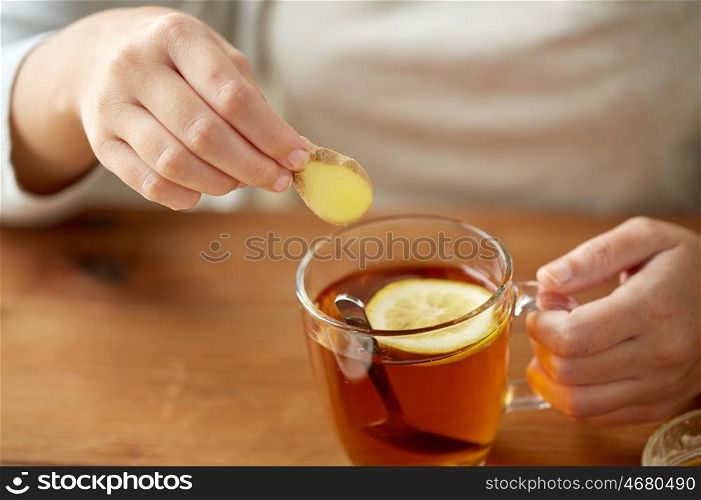 health, traditional medicine and ethnoscience concept - close up of woman adding ginger to tea cup with lemon