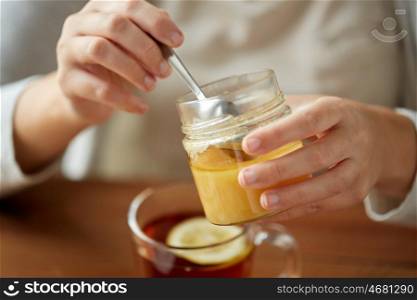health, traditional medicine and ethnoscience concept - close up of woman adding honey to tea with lemon