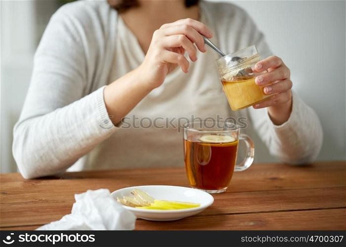 health, traditional medicine and ethnoscience concept - close up of woman adding honey to tea with lemon