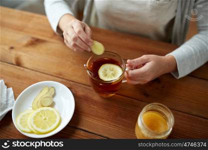 health, traditional medicine and ethnoscience concept - close up of woman adding ginger to tea cup with lemon and honey