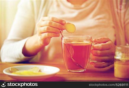 health, traditional medicine and ethnoscience concept - close up of woman adding ginger to tea cup with lemon and honey. close up of woman adding ginger to tea with lemon