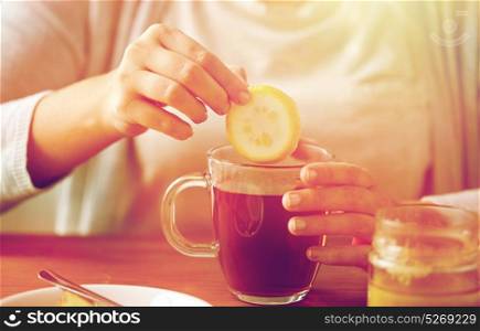 health, traditional medicine and ethnoscience concept - close up of woman adding lemon to tea cup with honey. close up of woman adding lemon to tea with honey