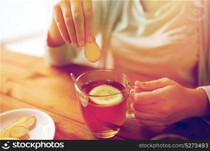 health, traditional medicine and ethnoscience concept - close up of woman adding ginger to tea cup with lemon. close up of woman adding ginger to tea with lemon