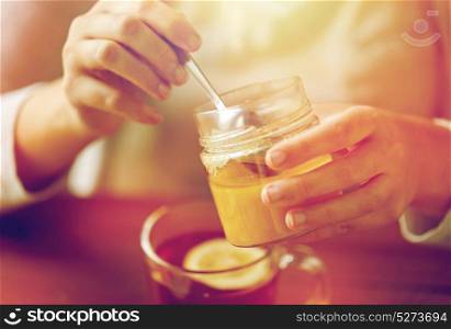 health, traditional medicine and ethnoscience concept - close up of woman adding honey to tea with lemon. close up of woman adding honey to tea with lemon