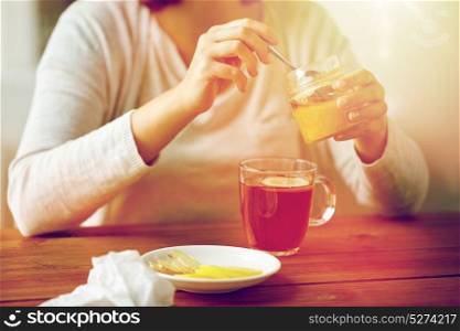 health, traditional medicine and ethnoscience concept - close up of woman adding honey to tea with lemon. close up of woman adding honey to tea with lemon