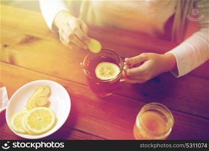 health, traditional medicine and ethnoscience concept - close up of woman adding ginger to tea cup with lemon and honey. close up of woman adding ginger to tea with lemon