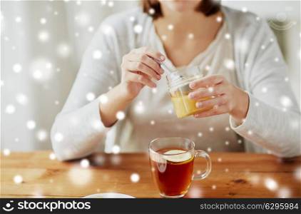 health, traditional medicine and ethnoscience concept - close up of woman adding honey to tea with lemon over snow. close up of woman adding honey to tea with lemon