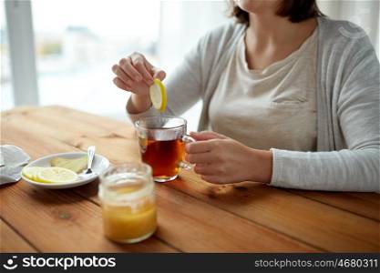 health, traditional medicine and ethnoscience concept - close up of woman adding lemon to tea cup