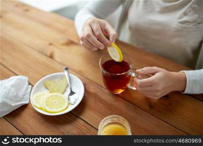 health, traditional medicine and ethnoscience concept - close up of woman adding lemon to tea cup