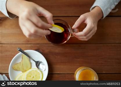 health, traditional medicine and ethnoscience concept - close up of woman adding lemon to tea cup. close up of woman adding lemon to tea cup