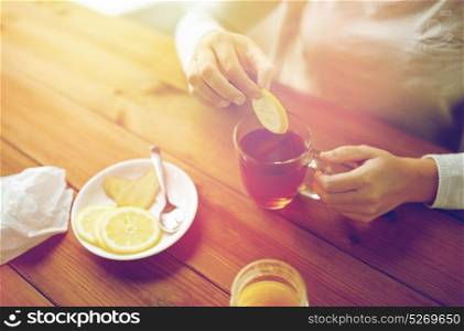 health, traditional medicine and ethnoscience concept - close up of woman adding lemon to tea cup. close up of woman adding lemon to tea cup