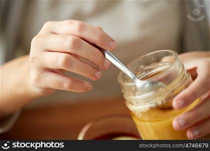 health, traditional medicine and ethnoscience concept - close up of woman hands with honey jar and spoon