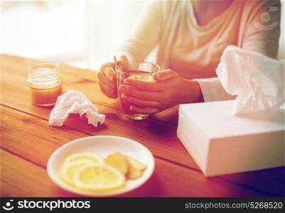 health, traditional medicine and ethnoscience concept - ill woman drinking tea with lemon and honey and paper wipes box on wooden table. ill woman drinking tea with lemon and honey