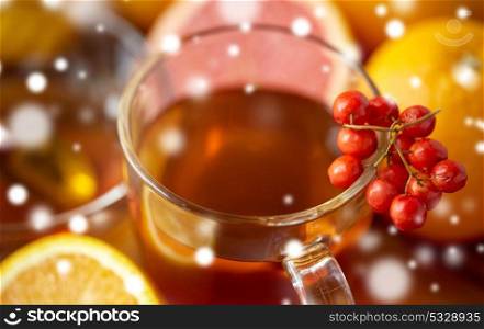 health, traditional medicine, folk remedy and ethnoscience concept - close up of tea cup with rowanberry over snow. close up of tea cup with rowanberry