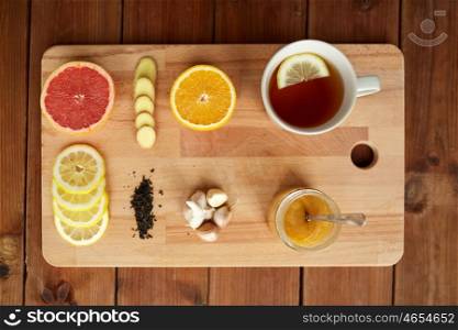 health, traditional medicine, folk remedy and ethnoscience concept - cup of ginger tea with honey, citrus and garlic on wooden board