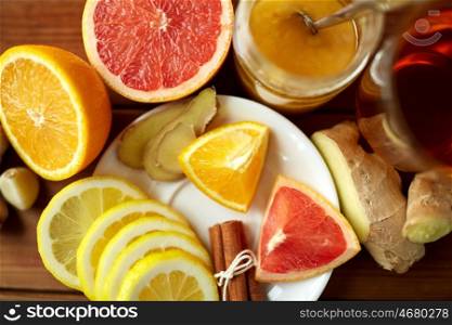 health, traditional medicine, folk remedy and ethnoscience concept - cup of ginger tea with honey, citrus and garlic on wooden background