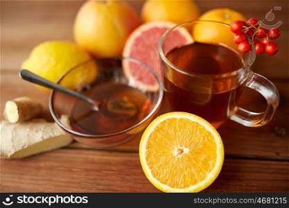 health, traditional medicine, folk remedy and ethnoscience concept - cup of ginger tea with honey, orange and rowanberry on wood