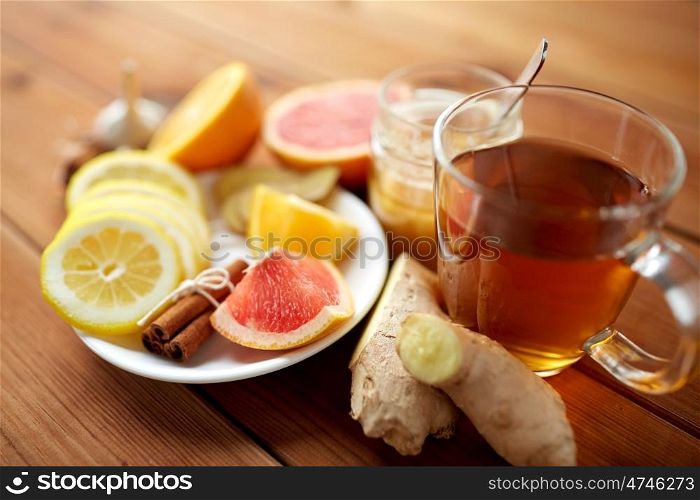 health, traditional medicine, folk remedy and ethnoscience concept - cup of ginger tea with honey, citrus and cinnamon on wooden background