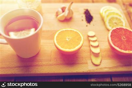 health, traditional medicine, folk remedy and ethnoscience concept - cup of ginger tea with honey, citrus and garlic on wooden background. ginger tea with honey, citrus and garlic on wood