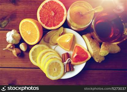 health, traditional medicine, folk remedy and ethnoscience concept - cup of ginger tea with honey, citrus and garlic on wooden background. ginger tea with honey, citrus and garlic on wood