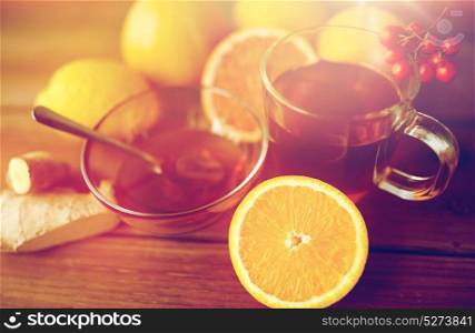 health, traditional medicine, folk remedy and ethnoscience concept - cup of ginger tea with honey, orange and rowanberry on wood. tea with honey, orange and rowanberry on wood