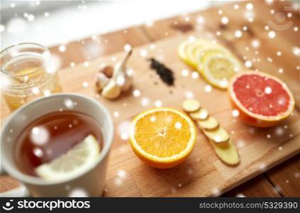 health, traditional medicine, folk remedy and ethnoscience concept - cup of ginger tea with honey, citrus and garlic on wooden board over snow. ginger tea with honey, citrus and garlic on wood