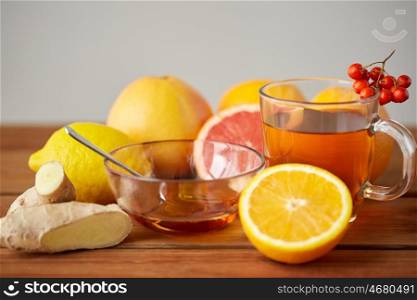 health, traditional medicine, folk remedy and ethnoscience concept - cup of tea with honey, lemon and ginger on wooden background