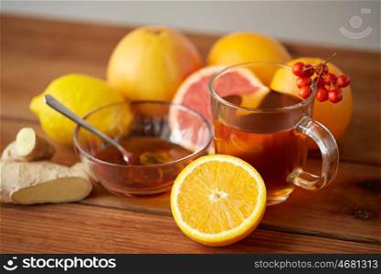 health, traditional medicine, folk remedy and ethnoscience concept - cup of tea with honey, lemon and ginger on wooden background