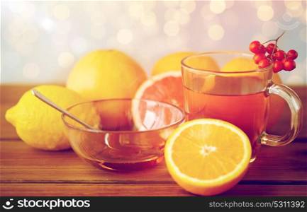 health, traditional medicine, folk remedy and ethnoscience concept - cup of tea with honey, lemon and rowanberry on wooden background. tea with honey, lemon and rowanberry on wood