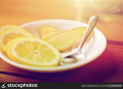health, traditional medicine, folk remedy and ethnoscience concept - lemon slices and chopped ginger on plate with spoon. lemon and ginger on plate with spoon