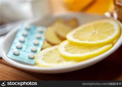 health, traditional medicine, folk remedy and ethnoscience concept - lemon slices, pills and ginger on plate