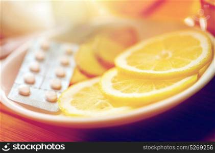 health, traditional medicine, folk remedy and ethnoscience concept - lemon slices, pills and ginger on plate. lemon slices, pills and ginger on plate
