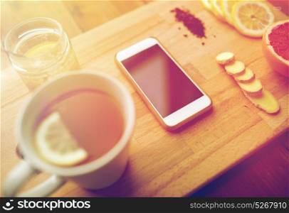 health, traditional medicine, folk remedy and ethnoscience concept - smartphone with cup of ginger tea, honey and citrus on wooden board. smartphone with cup of lemon tea, honey and ginger