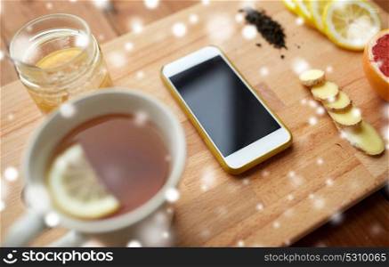 health, traditional medicine, folk remedy and ethnoscience concept - smartphone with cup of ginger tea, honey and citrus on wooden board over snow. smartphone with cup of lemon tea, honey and ginger