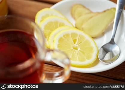 health, traditional medicine, folk remedy and ethnoscience concept - tea cup with lemon and ginger on plate with spoon