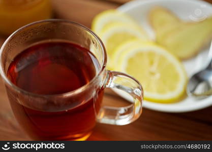 health, traditional medicine, folk remedy and ethnoscience concept - tea cup with lemon and ginger on plate with spoon