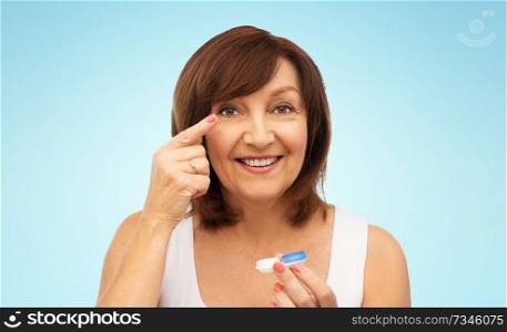 health, vision and old people concept - happy smiling senior woman putting on contact lenses over blue background. happy senior woman applying contact lenses