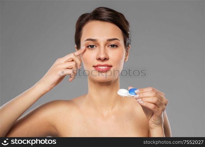 health, vision and old people concept - happy smiling young woman putting on contact lenses over grey background. happy young woman applying contact lenses