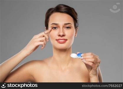 health, vision and old people concept - happy smiling young woman putting on contact lenses over grey background. happy young woman applying contact lenses