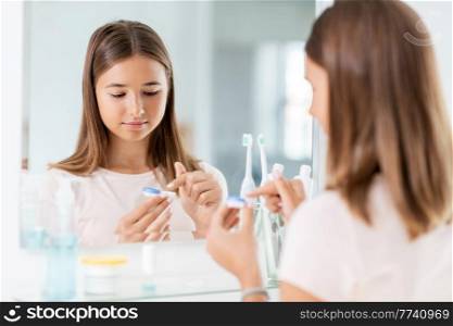 health, vision and old people concept - teenage girl applying contact lenses in front of mirror at home bathroom. teenage girl applying contact lenses at bathroom