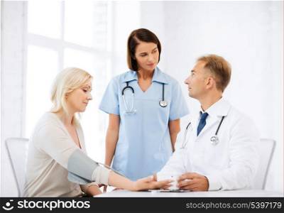 healthcare and medical concept - doctor and nurse with patient measuring blood pressure