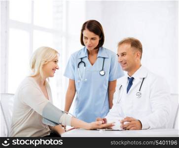 healthcare and medical concept - doctor and nurse with patient measuring blood pressure