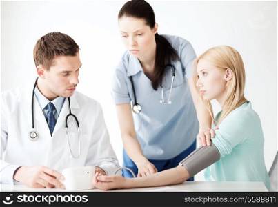healthcare and medical concept - doctor and nurse with patient measuring blood pressure in hospital